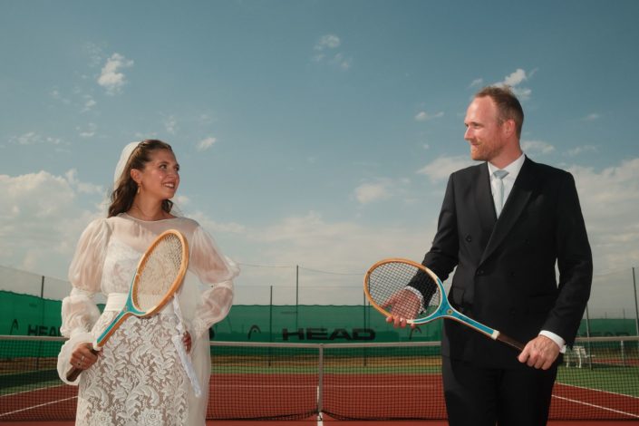 Les mariés jouent au tennis en tenue de mariage, moment complice et décalé